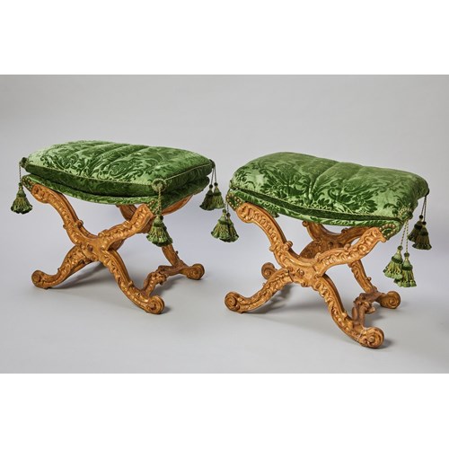 A pair of Italian giltwood carved folding stools, with a rectangular loose cushion seat, above an ‘X'-frame baluster supports, carved with scrolls, centred by a patera, joined by shaped stretchers centred by a stylised scallop-shell, on outward scrolled feet. Soon in a private collection in US